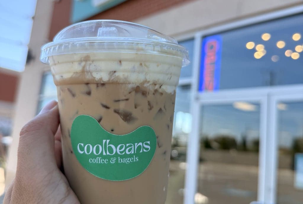 An iced cinnamon latte in a Coolbeans cup, held up outside the shop