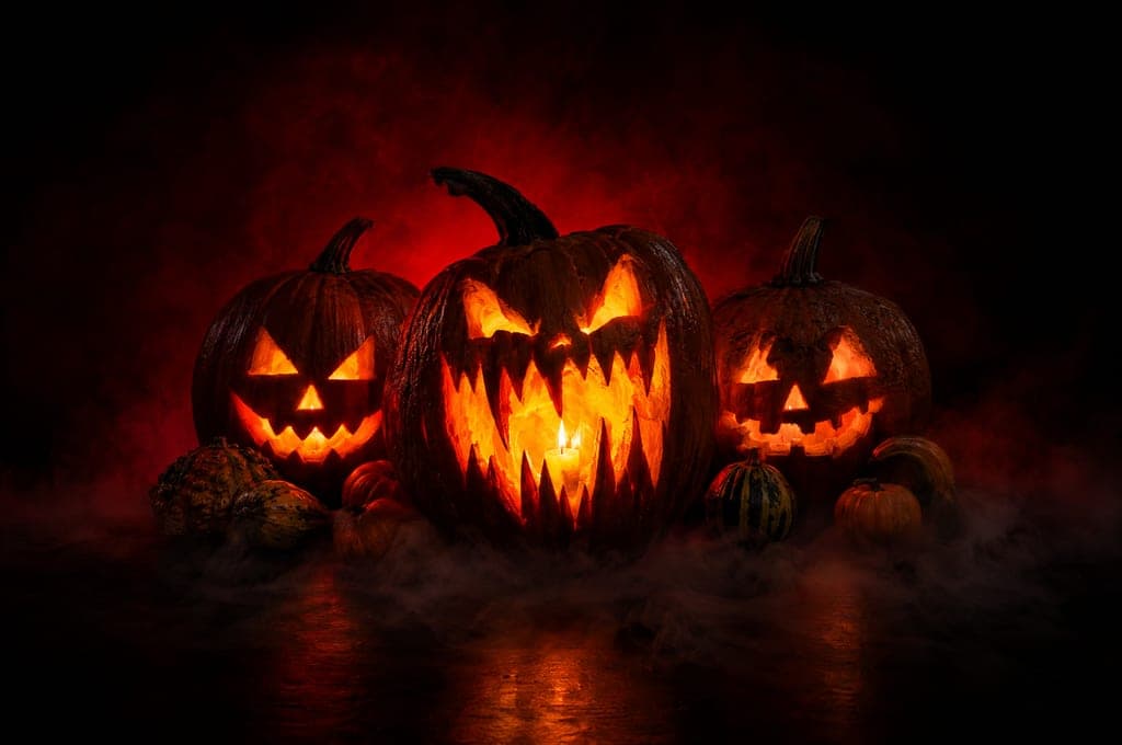 Three carved jack-o'-lanterns lit from inside, with small gourds