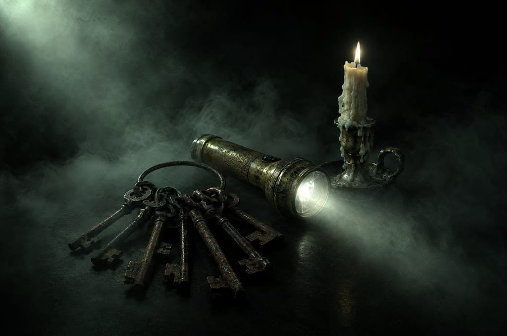 A ring of old skeleton keys, a flashlight and a melted candle in the dark